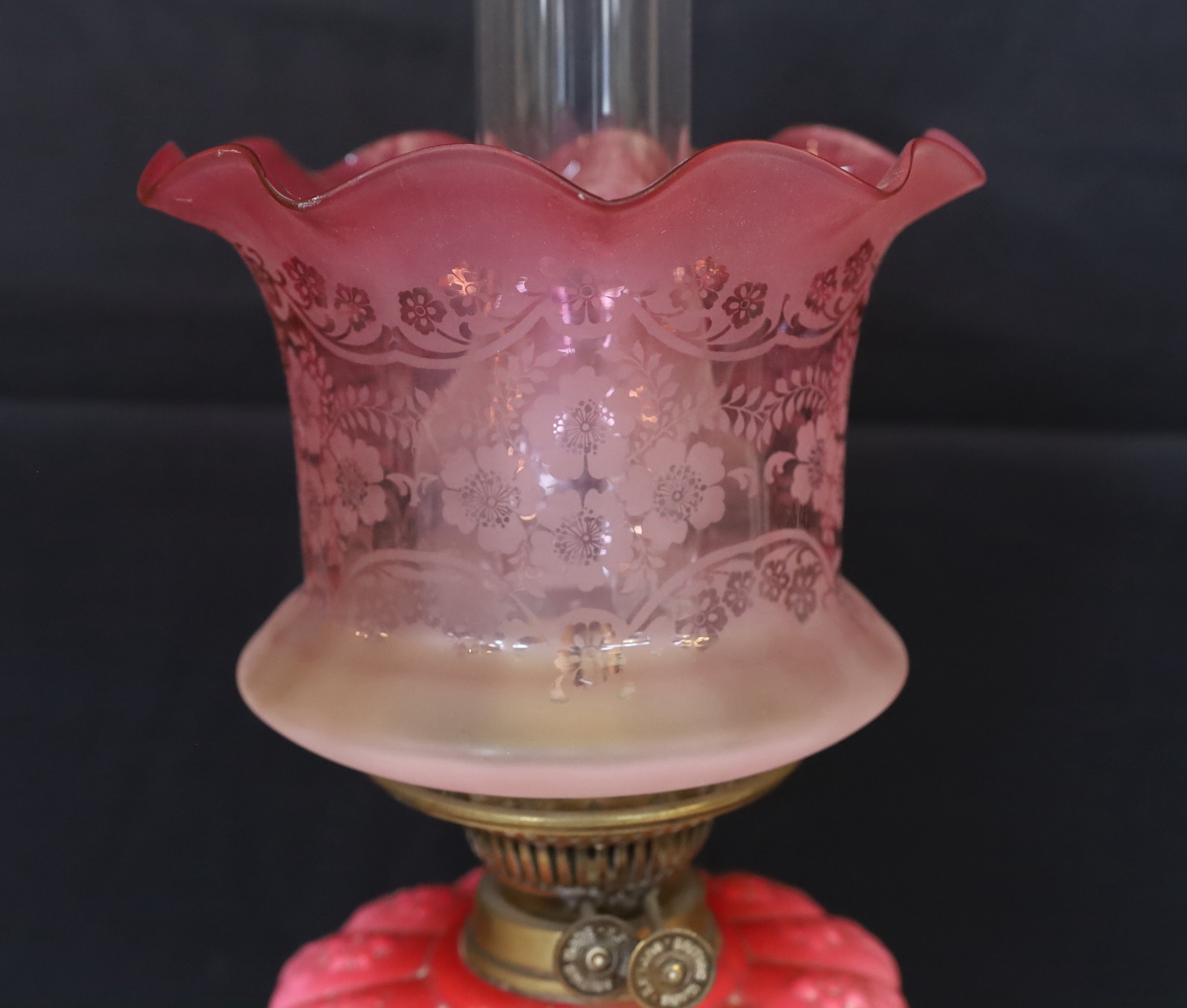 A late Victorian brass oil lamp with opaque pink glass reservoir, duplex mechanism, cranberry tinted etched glass shade and flue, height overall 65cm